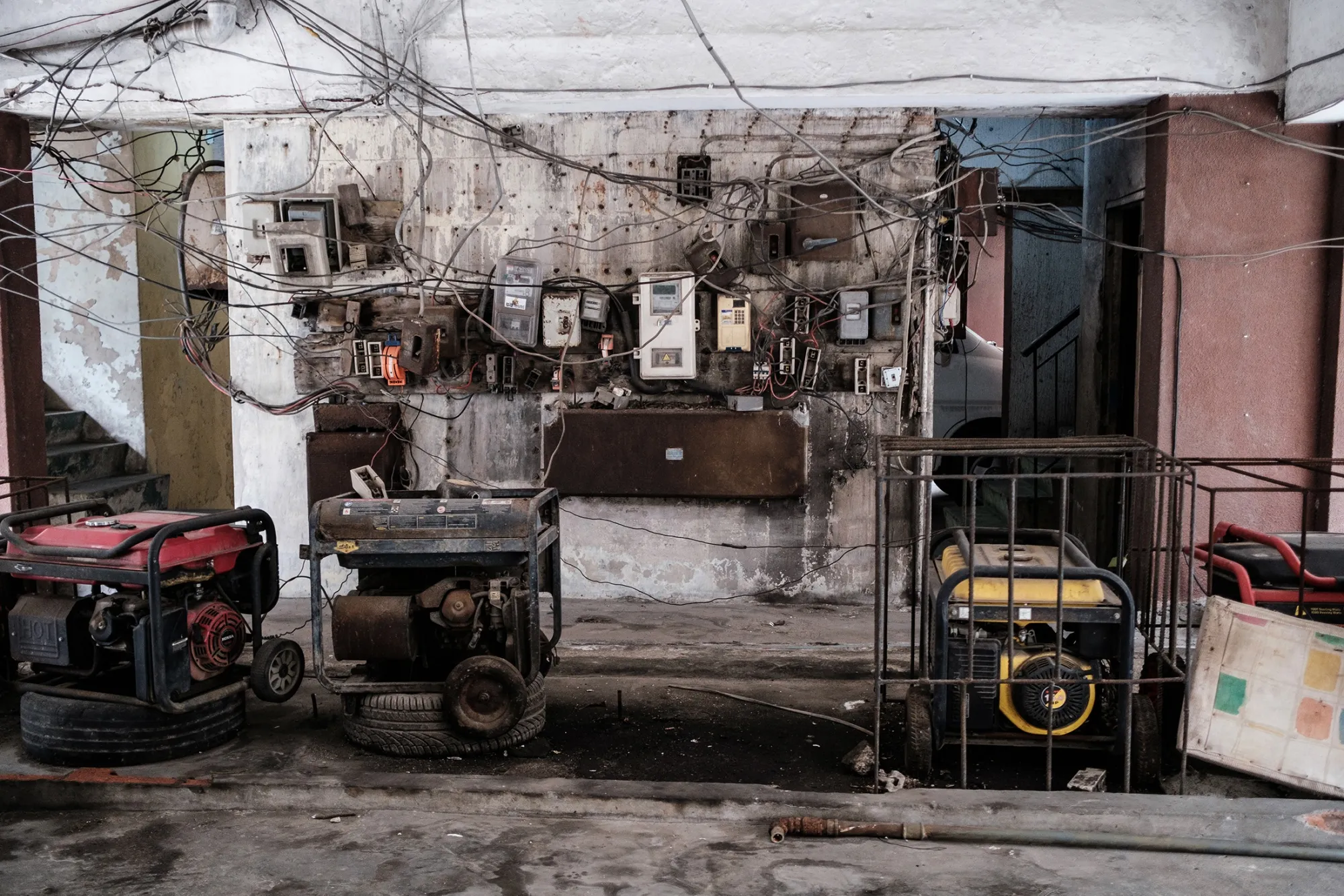 Several portable generators are lined up beneath a tangle of exposed electrical wires and meters in Lagos, used to compensate for unreliable power supply.