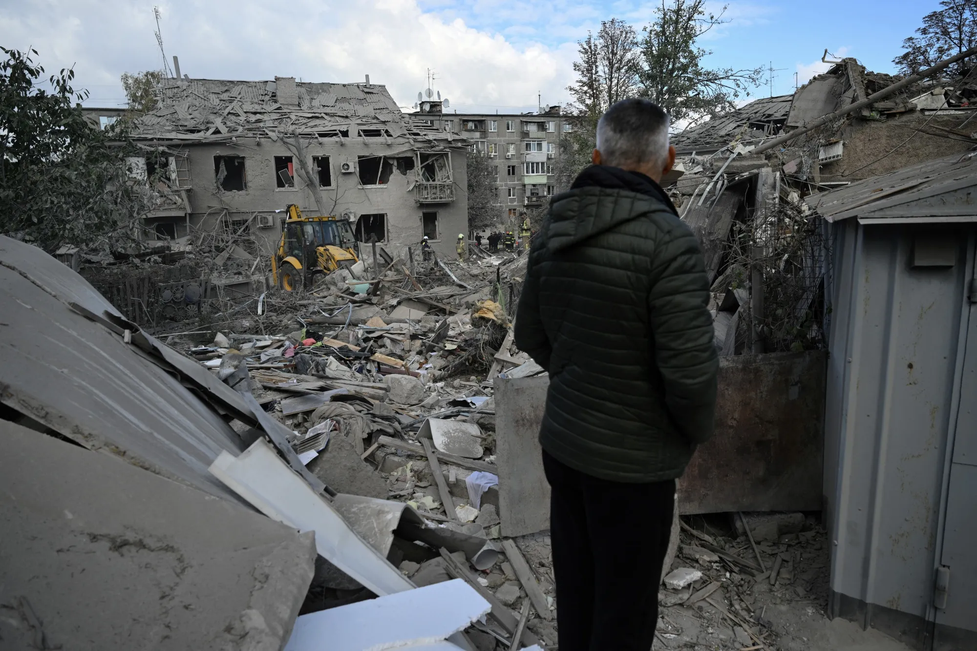 A local resident watches Ukrainian rescuers clear&nbsp;debris on the site of a Russian missile strike in Dnipro, Ukraine, on Oct. 26.