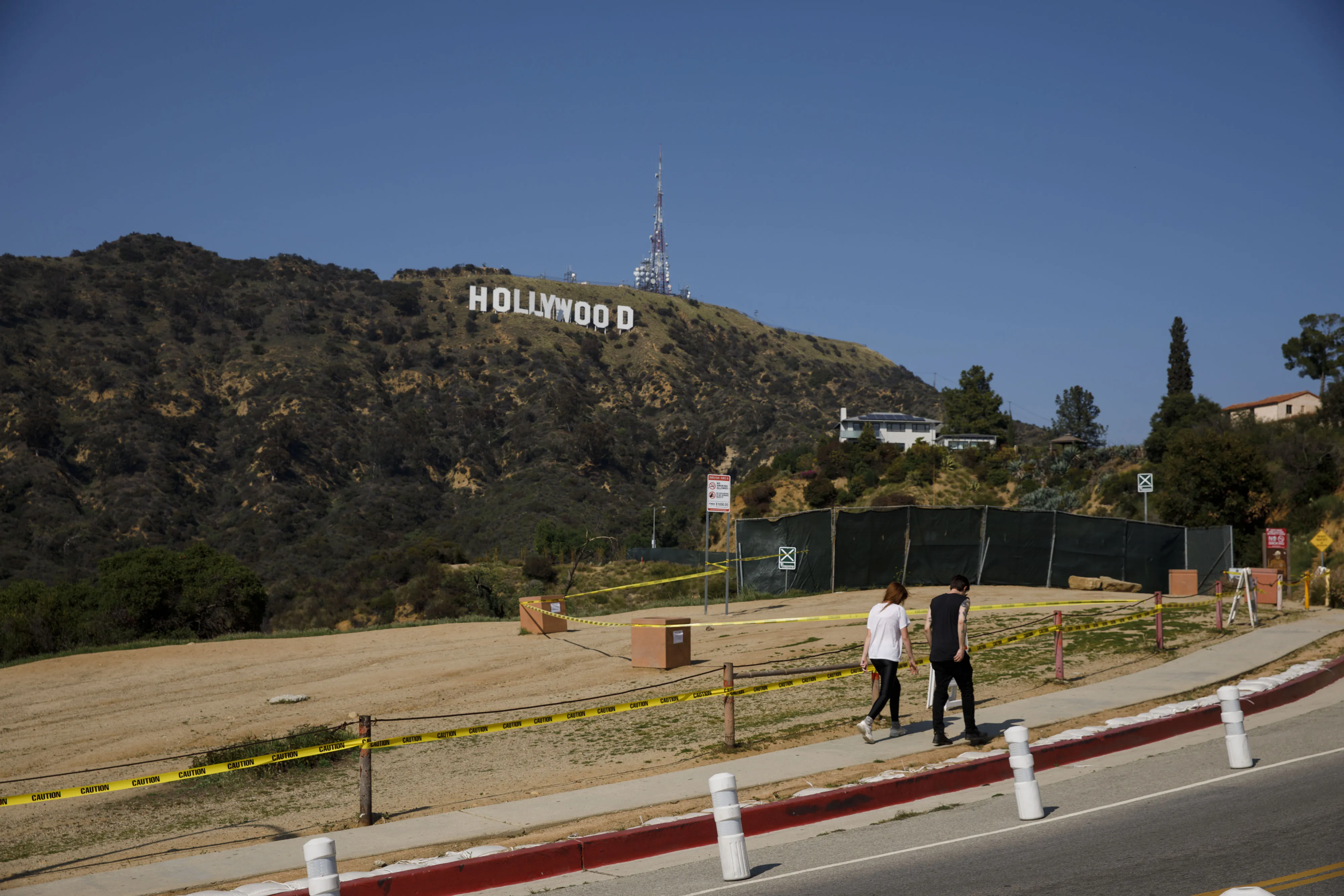 Pedestrians walk past fencing at Lake Hollywood Park below the Hollywood sign in Los Angeles, California, U.S., on Wednesday, April 1, 2020.&nbsp;