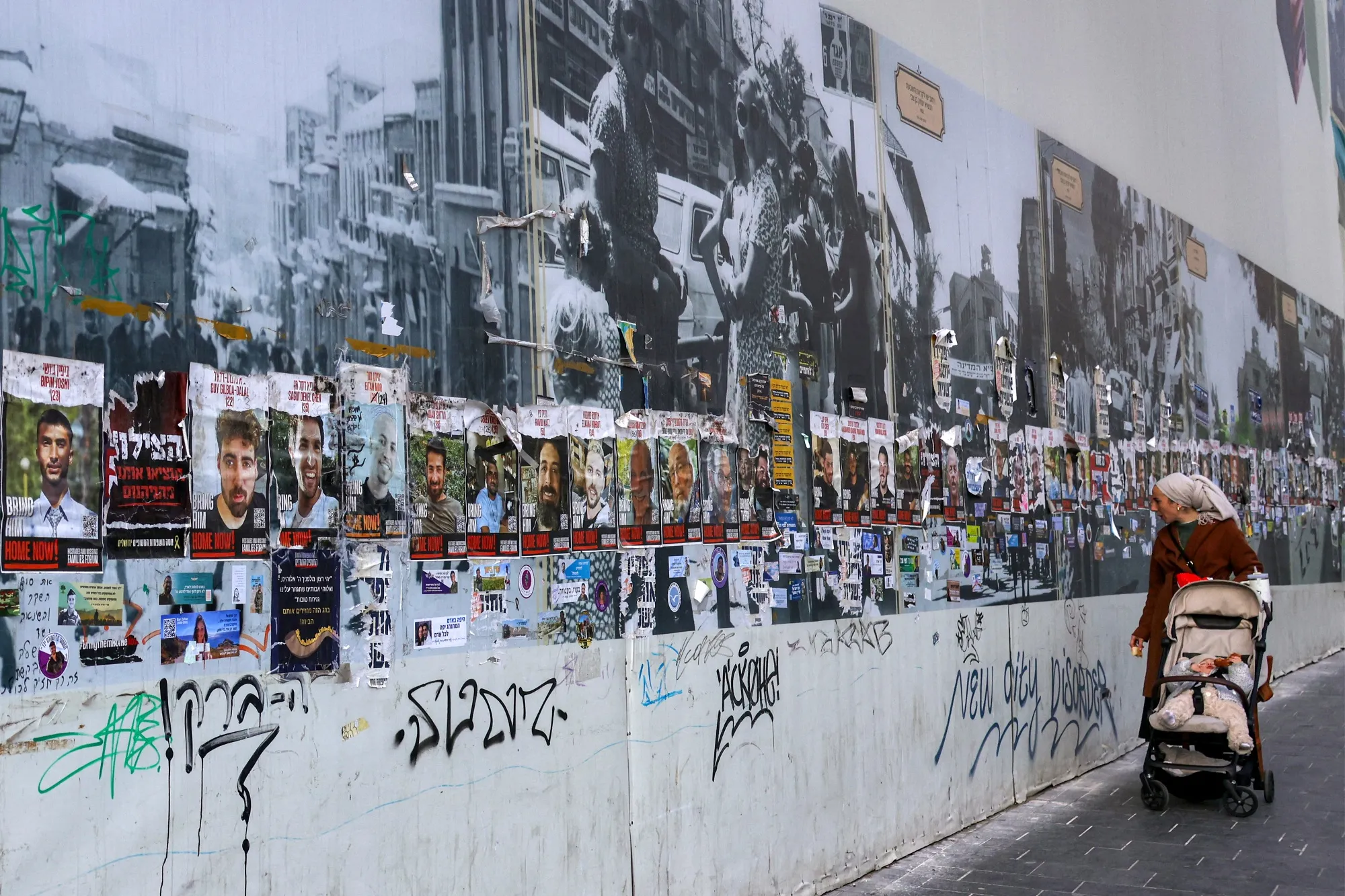 A woman pushing a child stroller views some of the posters depicting pictures of Israeli hostages taken captive in the Gaza.