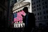 A pedestrian views a mobile device while walking past an American flag displayed outside of the New York Stock Exchange (NYSE) in New York, U.S..