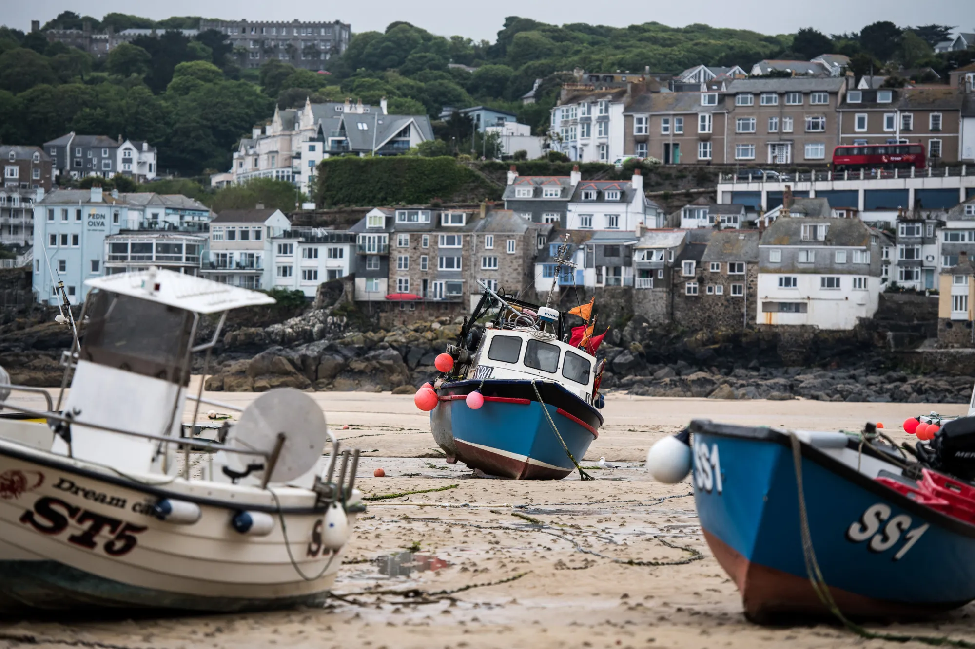 Fishing boats sit moored on the sea bed at low tide in the harbor in St. Ives.
