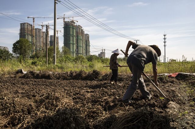 Farmers tend to vegetable plot near high-rise apartment buildings at China Evergrande Group's under-construction Riverside Palace development in Taicang, Jiangsu province, China, on Friday, Sept. 24, 2021. China's housing regulator has stepped up oversight of China Evergrande Group's bank accounts to ensure funds are used to complete housing projects and not diverted to pay creditors.