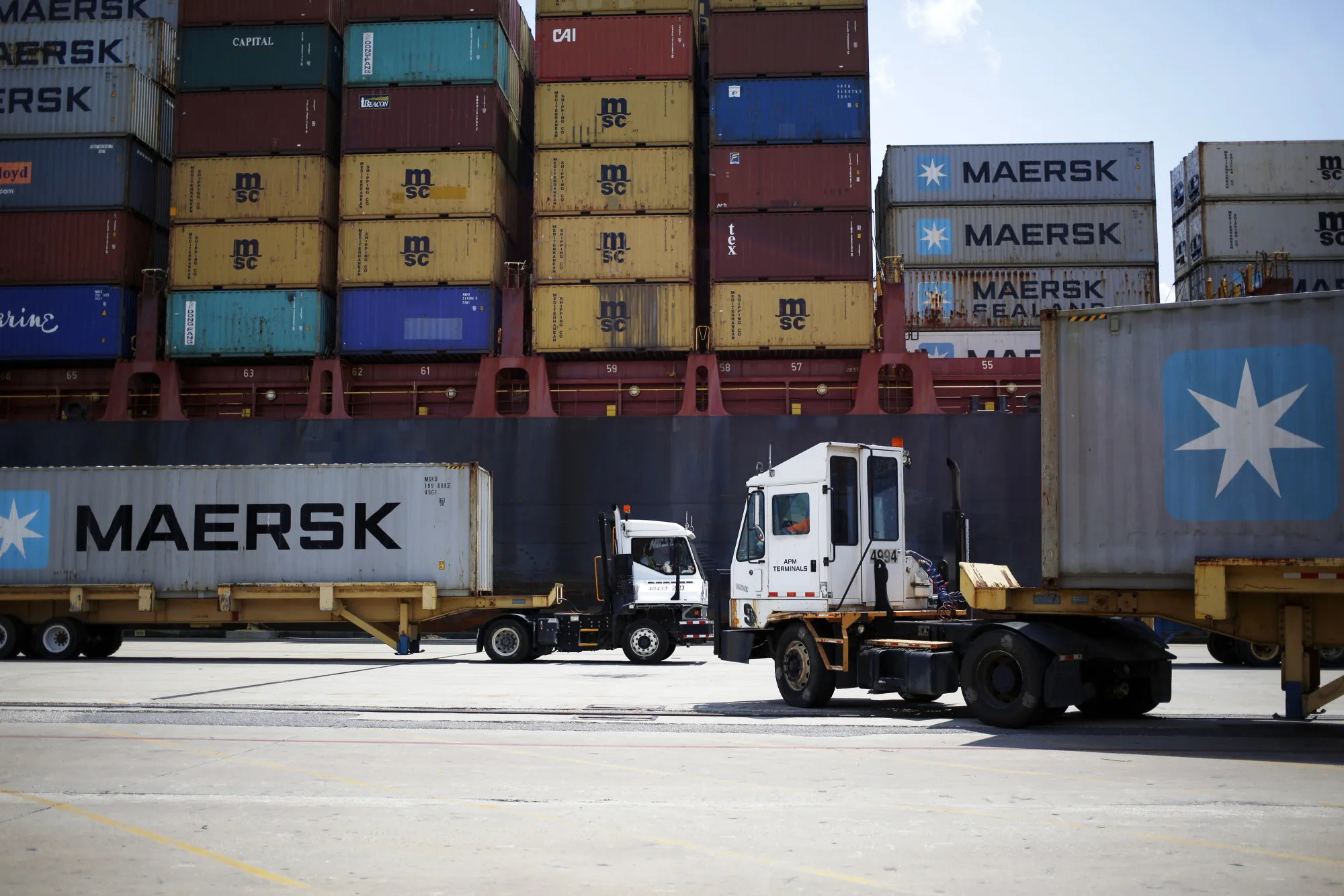 Trucks carry shipping containers next to a cargo ship docked in the APM Terminals yard at the Port of Mobile in Mobile, Alabama, U.S., on Thursday, July 20, 2017. The U.S. Census Bureau released trade balance of goods and services figures on August 4.