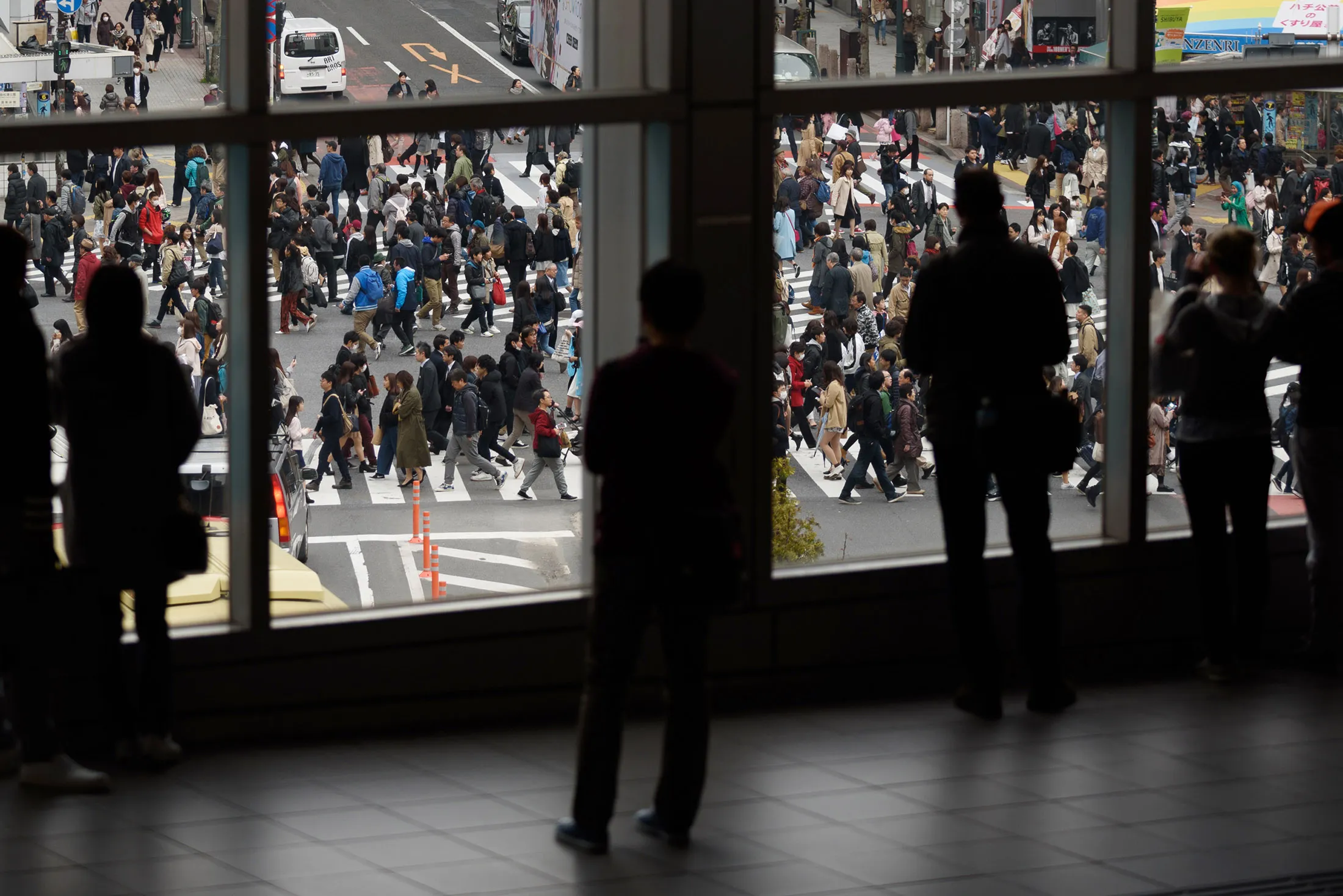 People are silhouetted as they stand on a footbridge overlooking pedestrians crossing an intersection in the Shibuya district of Tokyo.