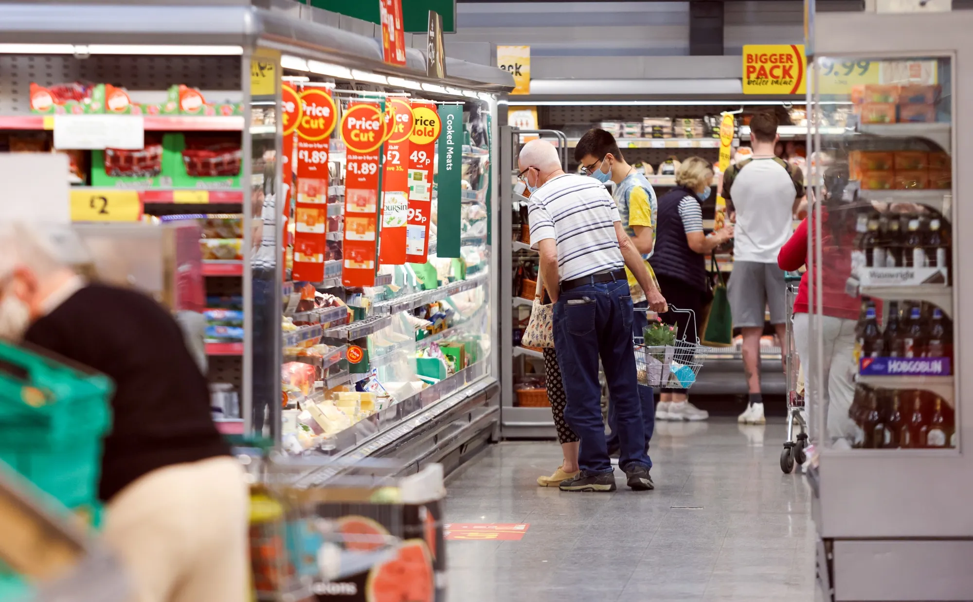 Customers browse a refrigerated aisle of food at a Morrisons supermarket in Saint Ives, U.K.