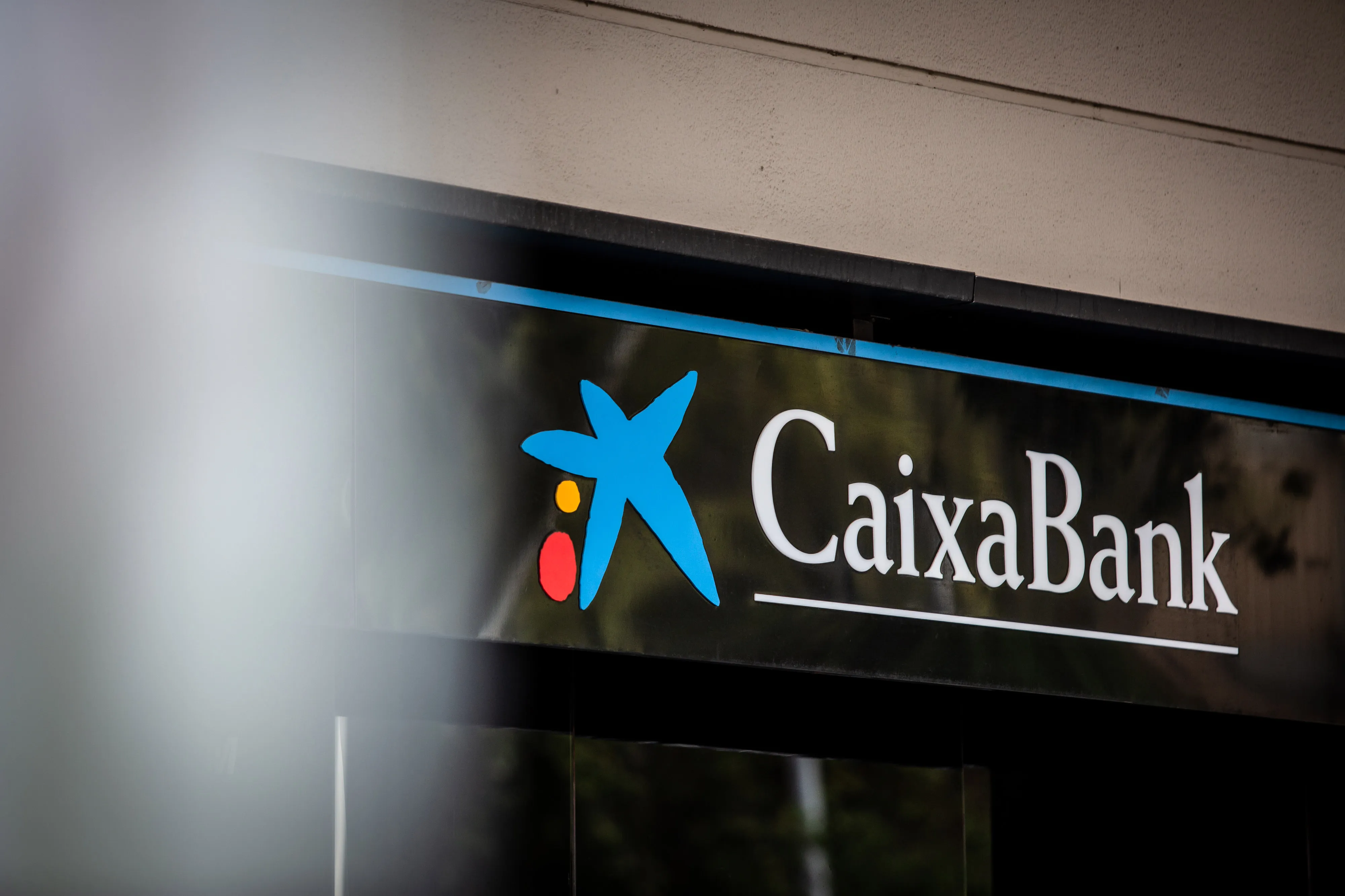 Signage above the entrance to a Caixabank SA bank branch in Barcelona.