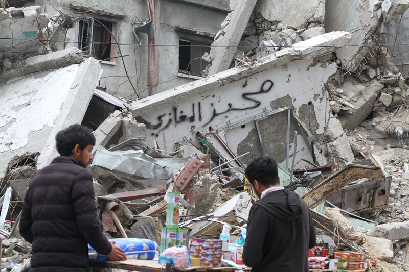 Palestinians sell goods on a roadside beside a destroyed building in the Al-Maghazi camp in central Gaza Strip