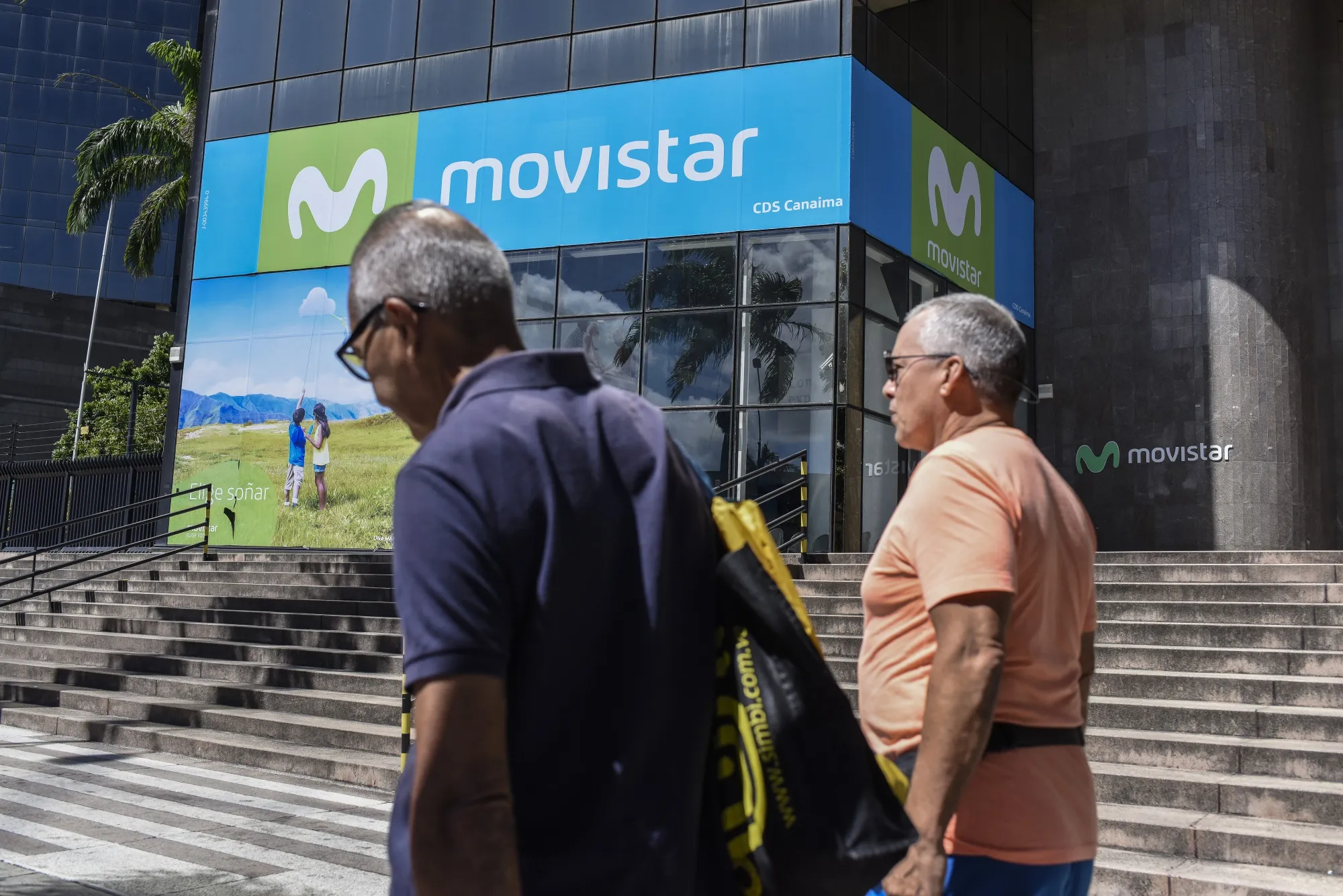 Pedestrians pass in front of Telefonica Movistar headquarters in the Los Palos Grandes district in Caracas, Venezuela, on Saturday, Dec. 8, 2018. 