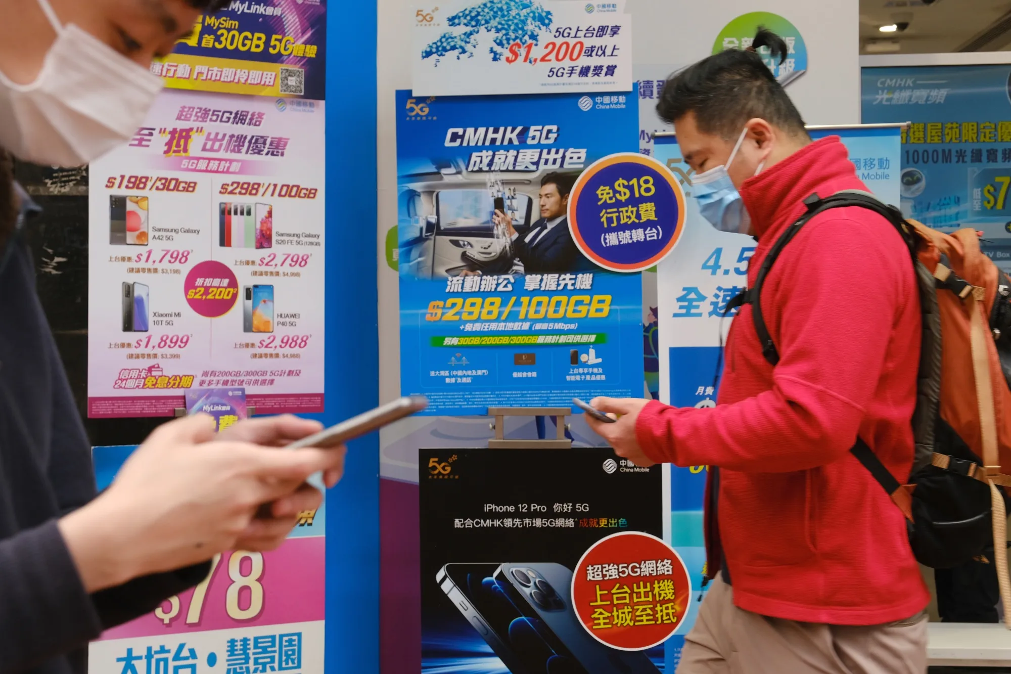 Pedestrian wearing protective masks walk past advertisements at a China Mobile Ltd. store in Hong Kong.