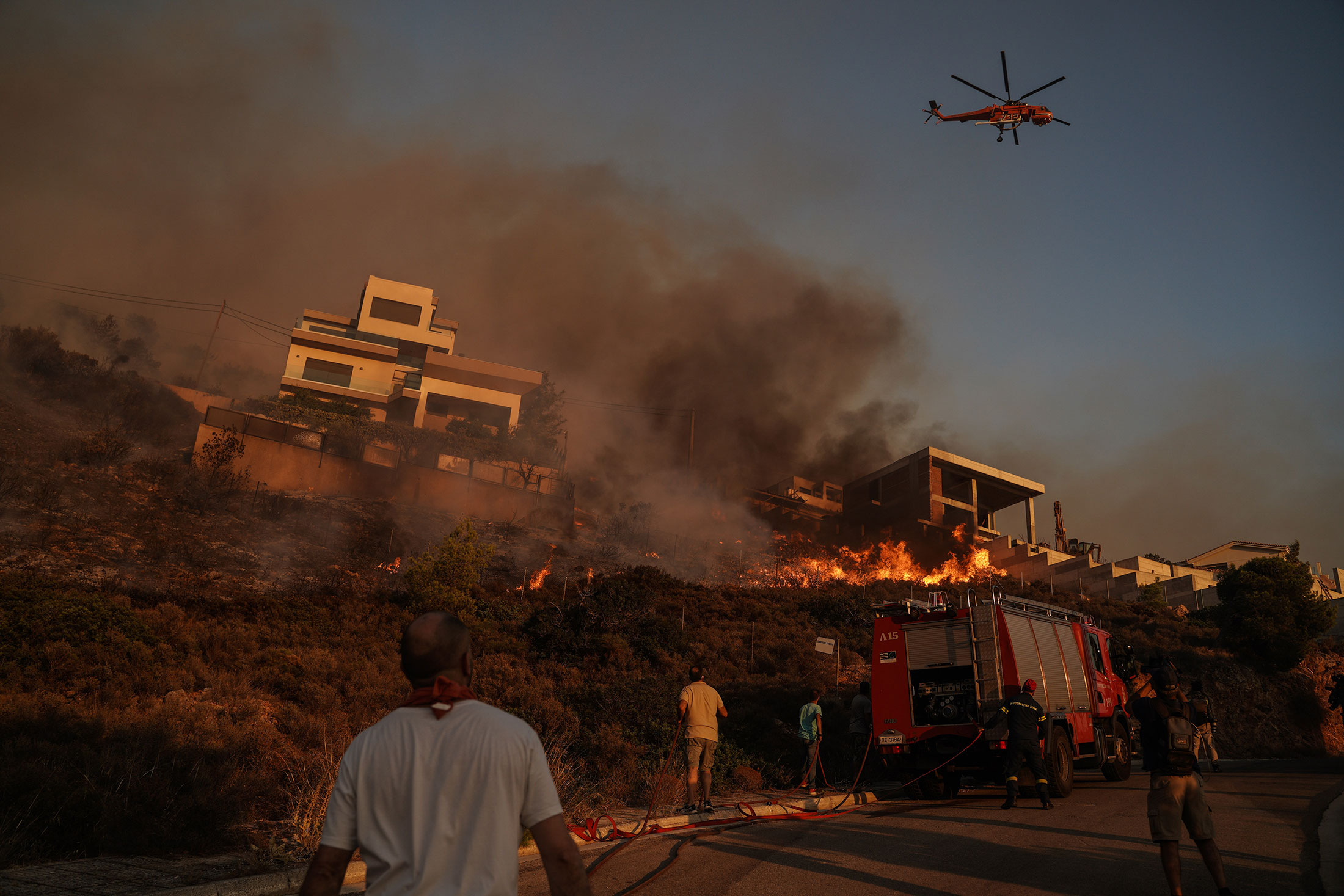Firefighters and volunteers work to extinguish a burning building during a wildfire in Saronida, south of Athens, Greece, on Monday, July 17, 2023. 