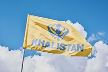A yellow Khalistan flag with blue-type flying outdoors.