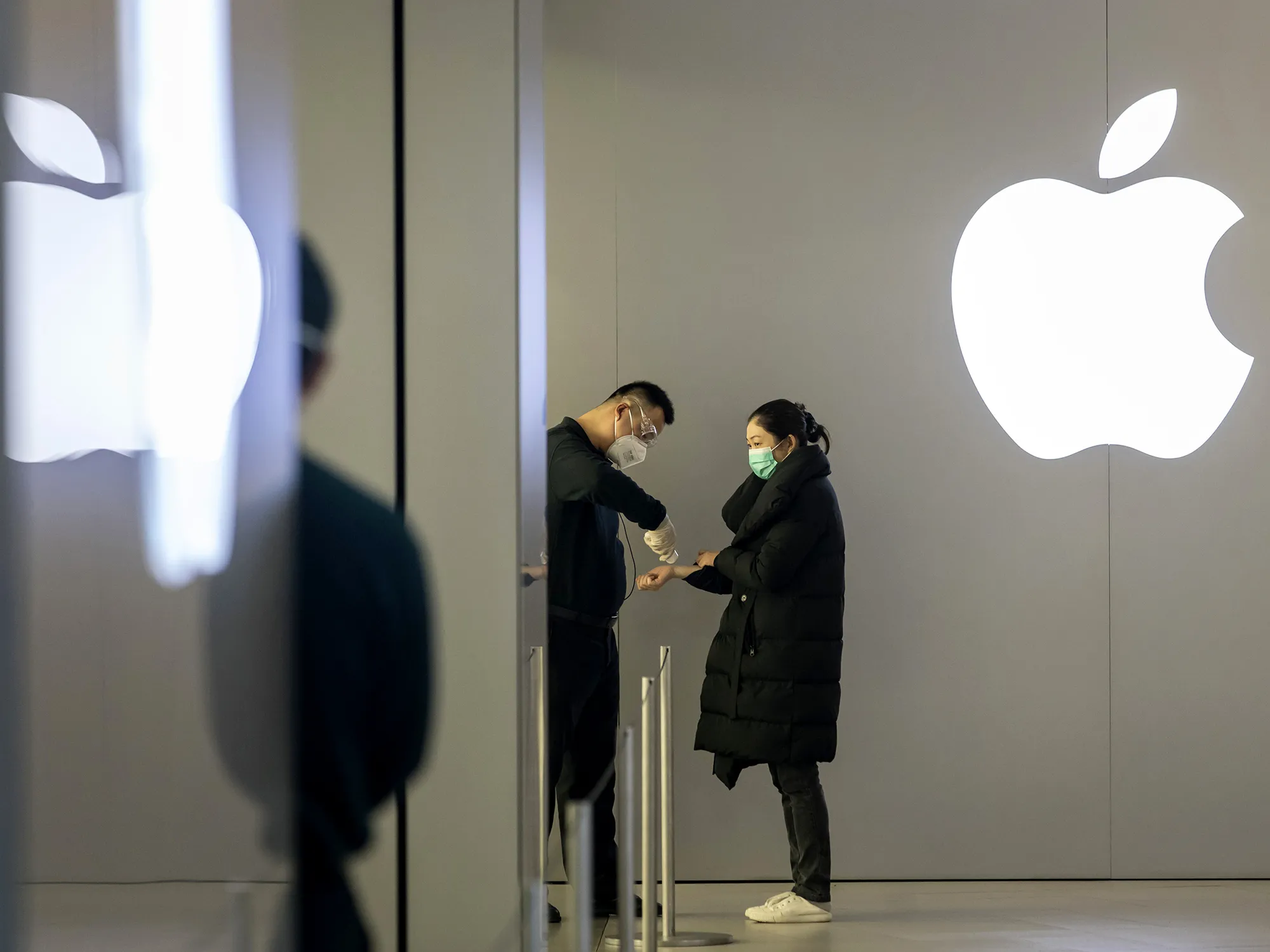 An employee wearing a protective mask takes the temperature of a customer at an entrance to an Apple store in Shanghai.