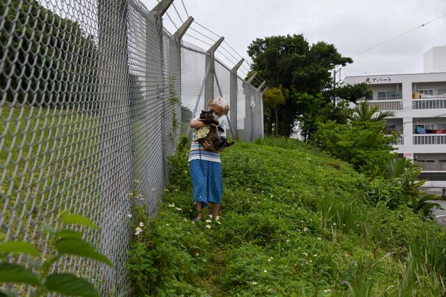A woman with a cat next to the fence of the Futenma airfield.