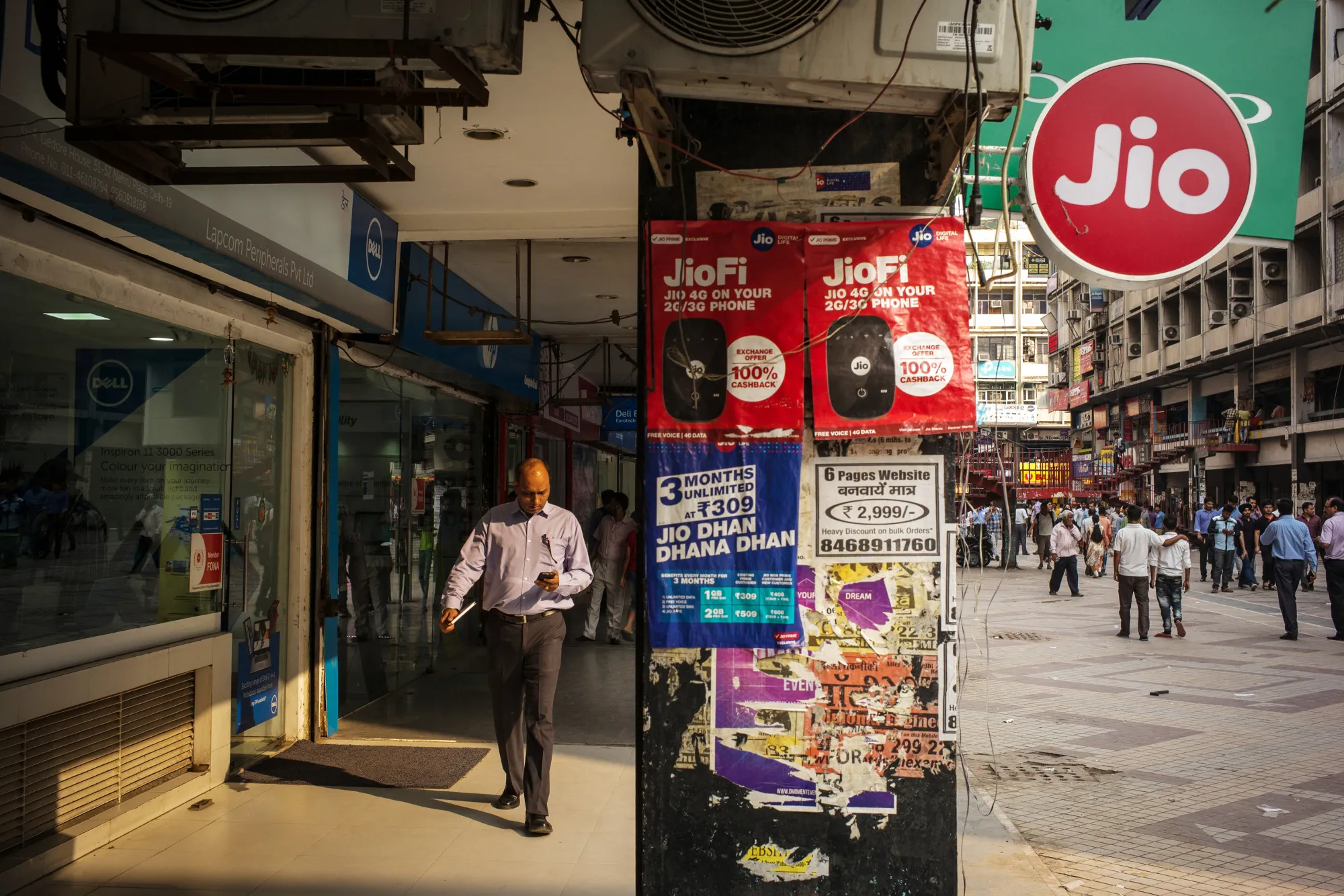 A pedestrian using a smartphone walks past advertising and signage for Reliance Jio Infocomm Ltd. at the Nehru Place IT Market in New Delhi.
