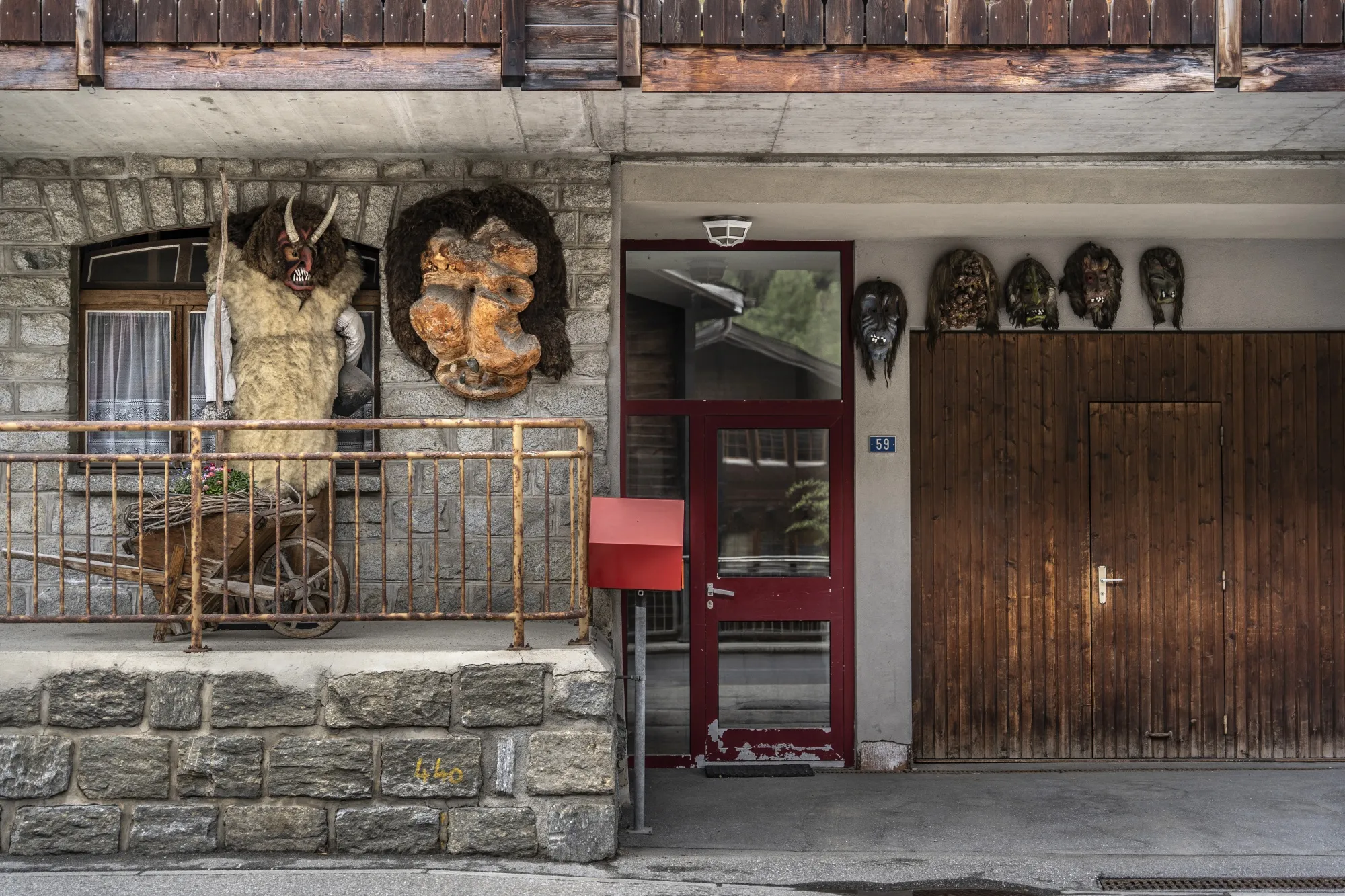 Masks hang outside a building and a monster with fur and horns holds a stick on a raised patio.