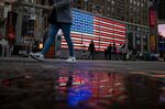 Pedestrians walk past an illuminated American flag in the Times Square area of New York.