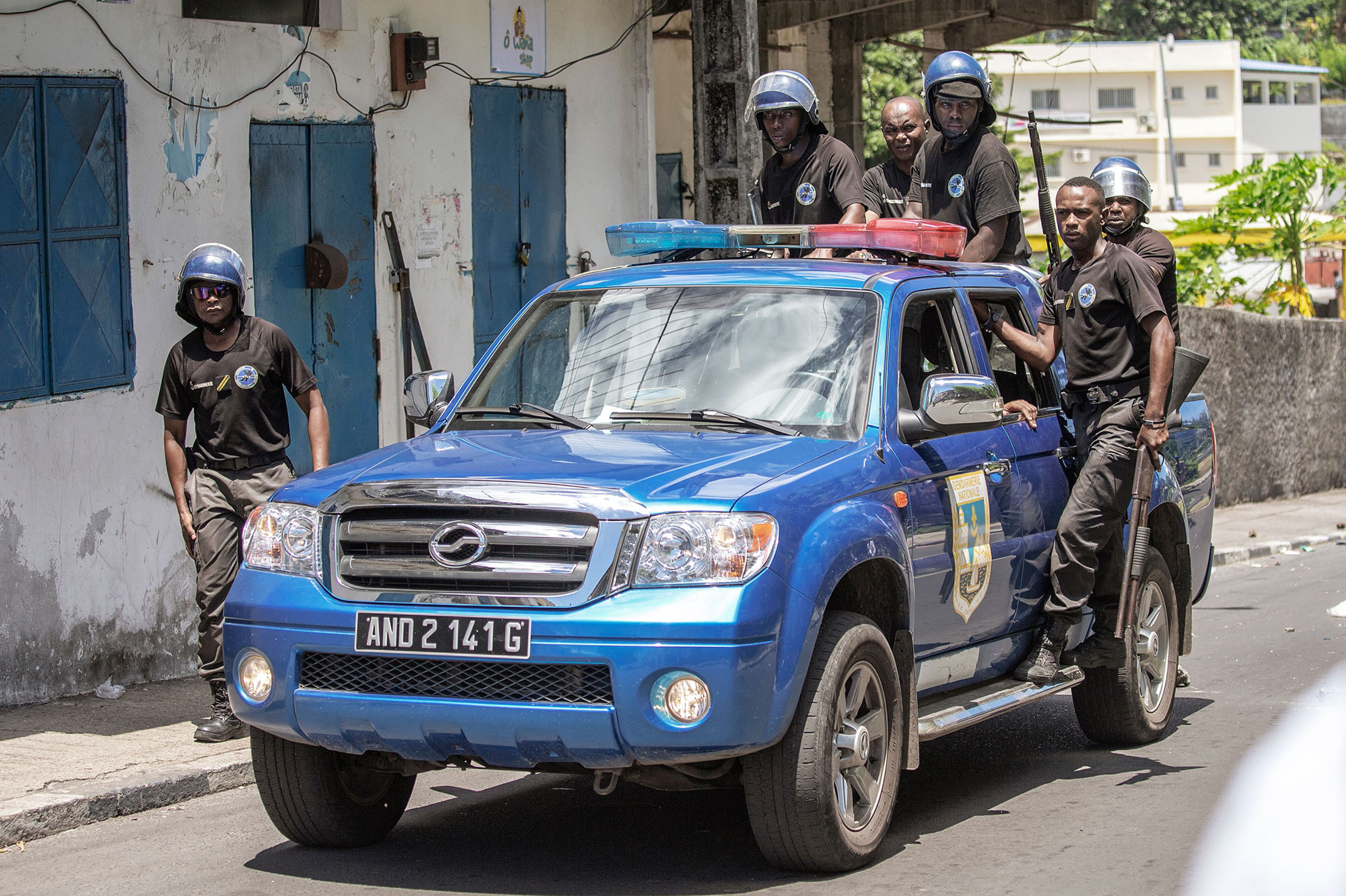 Comoros Gendarmerie officers stand on the back of a car as they disperse opposition supporters, in Moroni, on March 25.