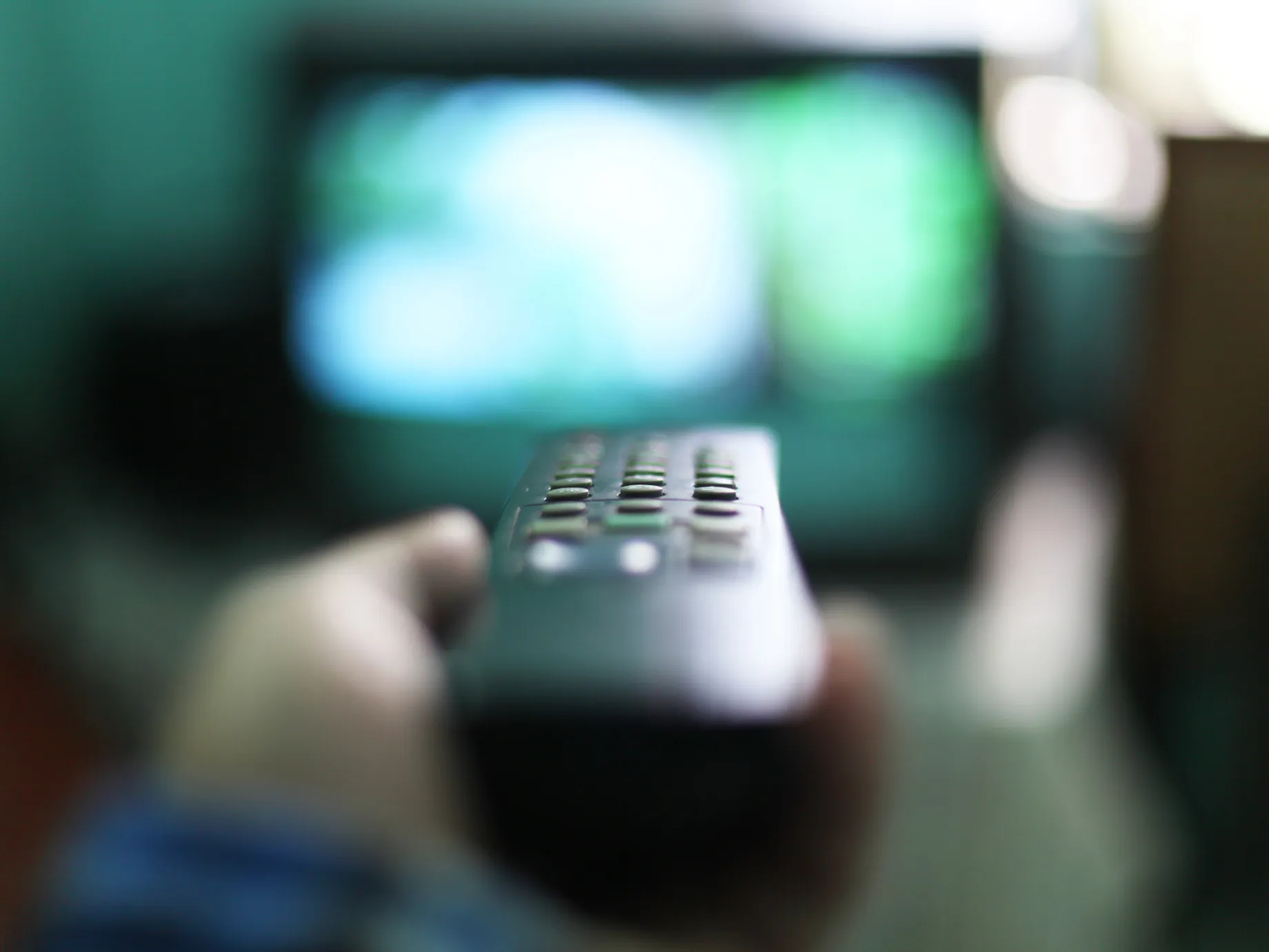 Human hand holding remote control in front of t.v.