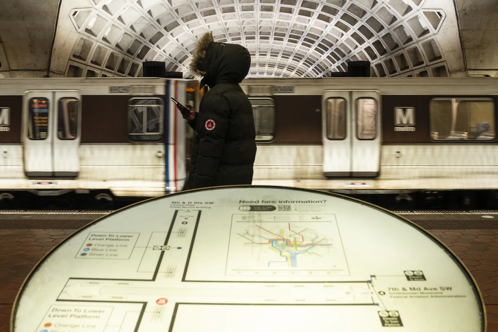 A commuter talks on a cell phone while waiting for a train at L'Enfant Plaza station in Washington, DC, in 2023. The Metro station’s is getting a lot of new&nbsp;signage.&nbsp;