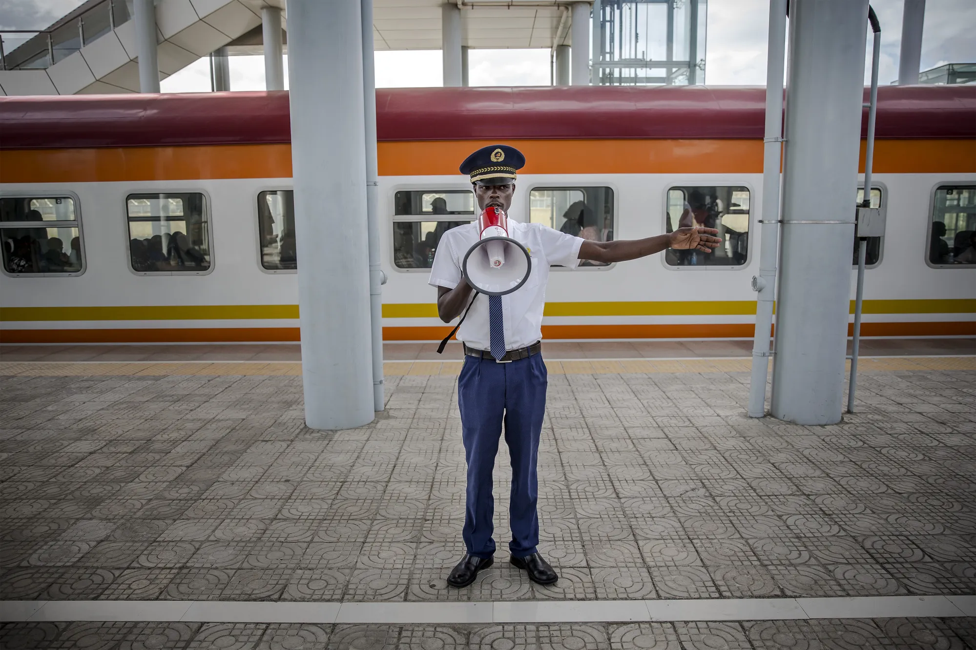 A train guard uses a megaphone to instruct rail travelers on a platform at Mombasa SGR Terminus station.