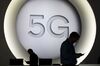 Attendees check their smartphone devices by a 5G sign during the opening day of the Mobile World Congress (MWC).
