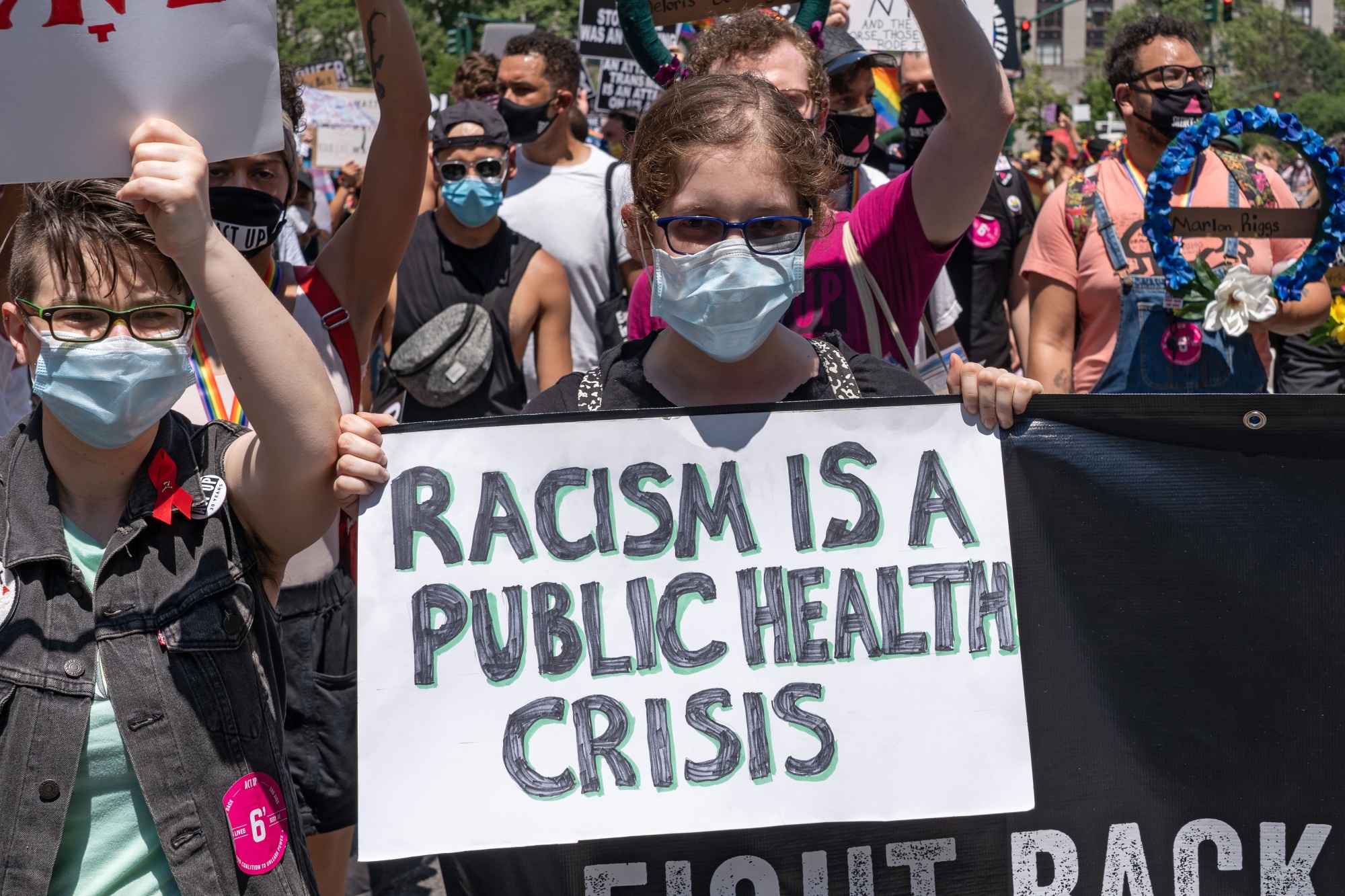 A participant holds a placard that says “racism is a public health crisis” in Foley Square during the Queer Liberation March in lower Manhattan on June 28. Cities, school districts, and health agencies are making this statement official policy by passing declarations.&nbsp;
