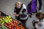 A customer counts coins to pay on a fresh produce stall at the market in the Plaza Mayor of Vic, Spain.