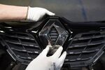 A worker attaches a Renault diamond badge to the front grille of an automobile&nbsp;inside a&nbsp; Renault SA automobile plant.