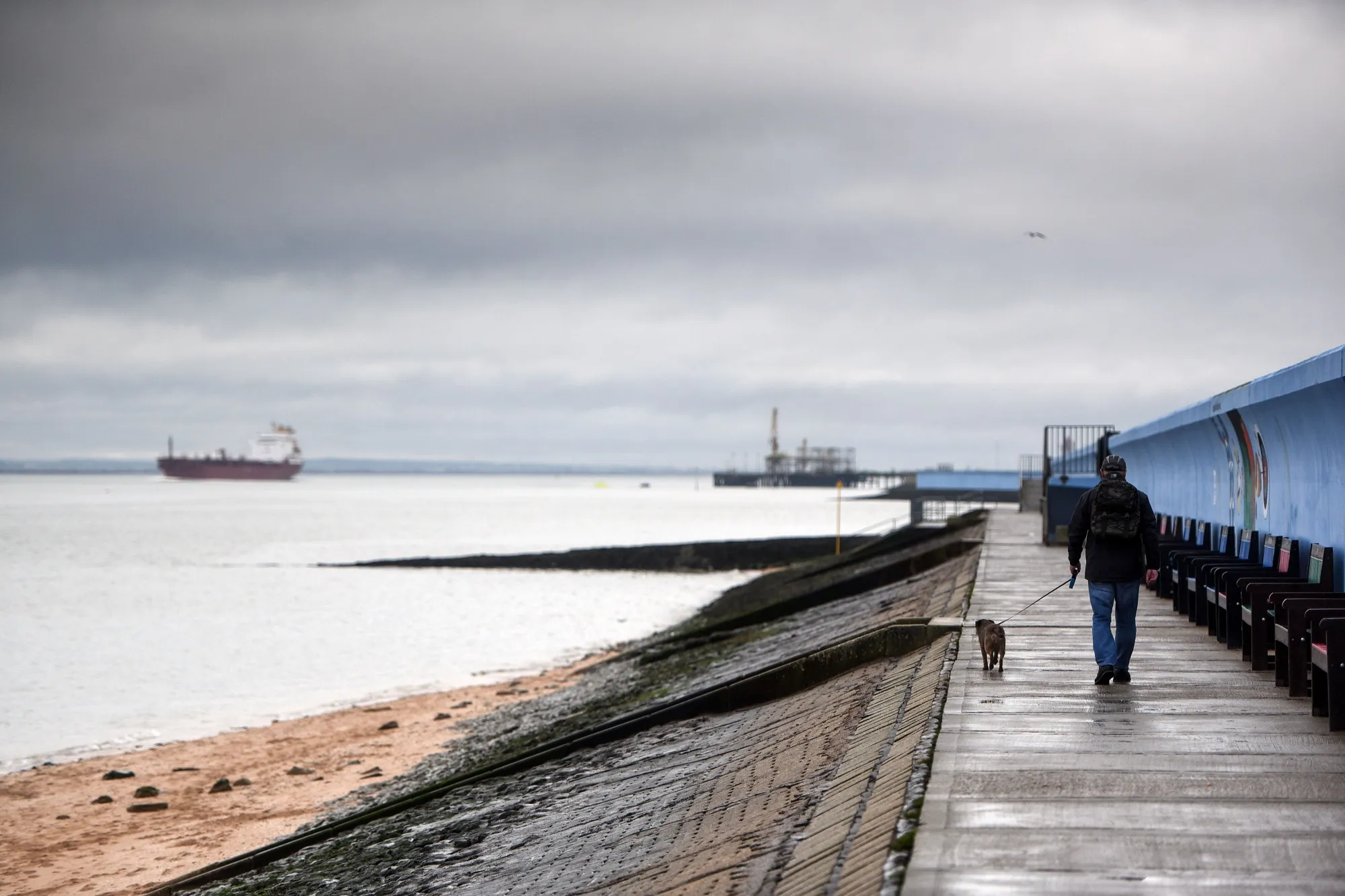 A pedestrian walks his dog along sea defence wall on Canvey Island, UK, on Thursday, Jan 30, 2020.&nbsp;