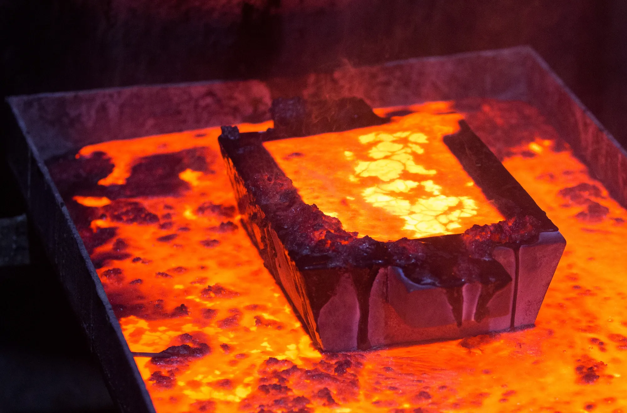A casting mold filled with molten gold sits above a melting vat during the manufacture of gold ingots.