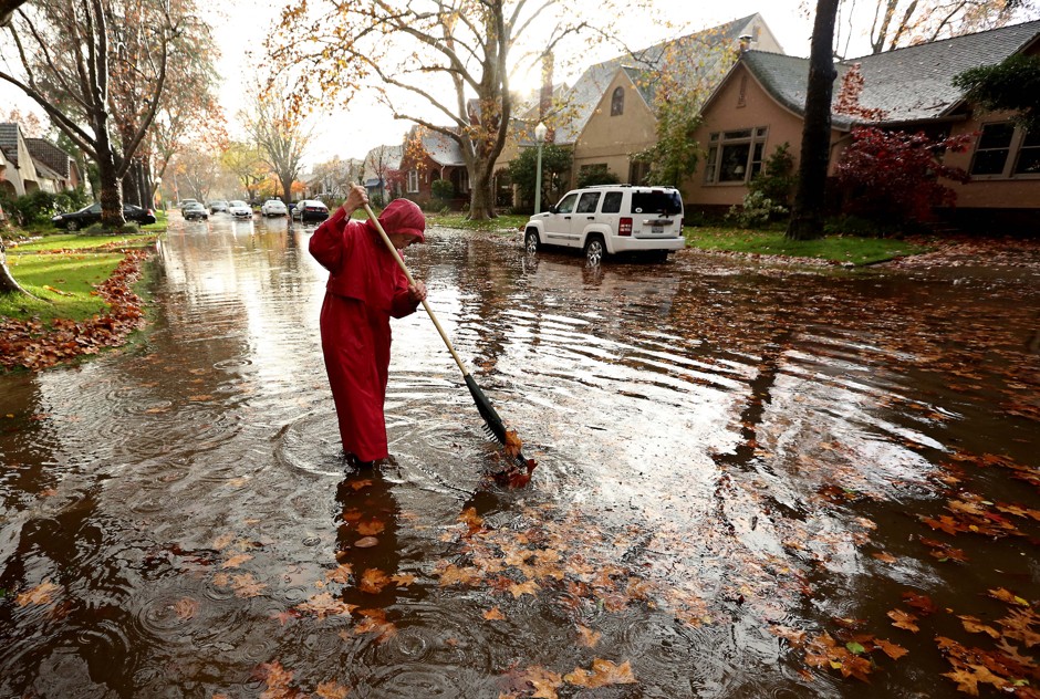 Marilyn Van Schenk stands in knee-deep water as she clears a clogged storm drain that had caused her street to flood in Sacramento.