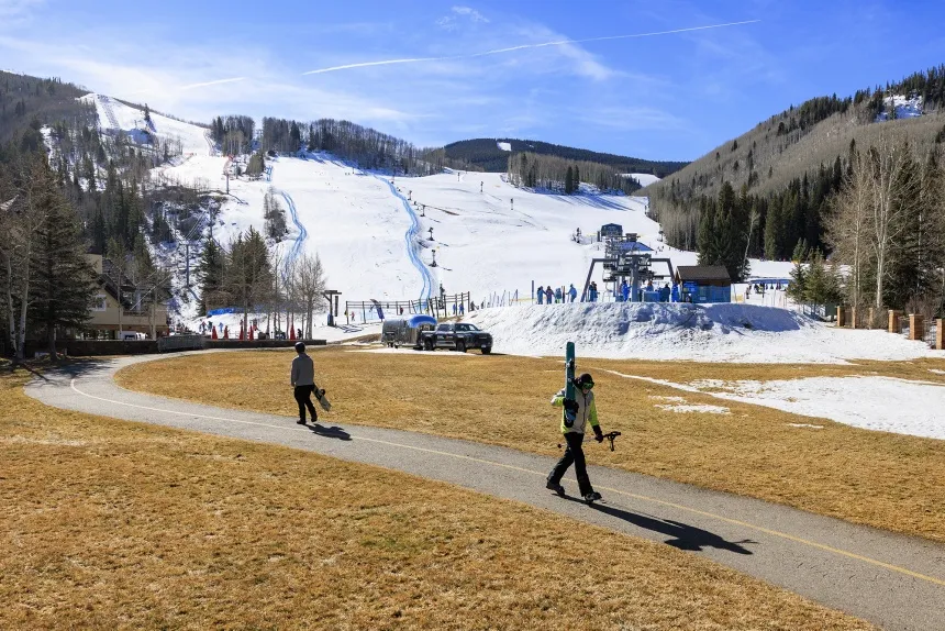 A skier and snowboarder walk through a grassy field to the chairlift at Vail Ski Resort&nbsp;in Vail, Colorado on March 18.&nbsp;