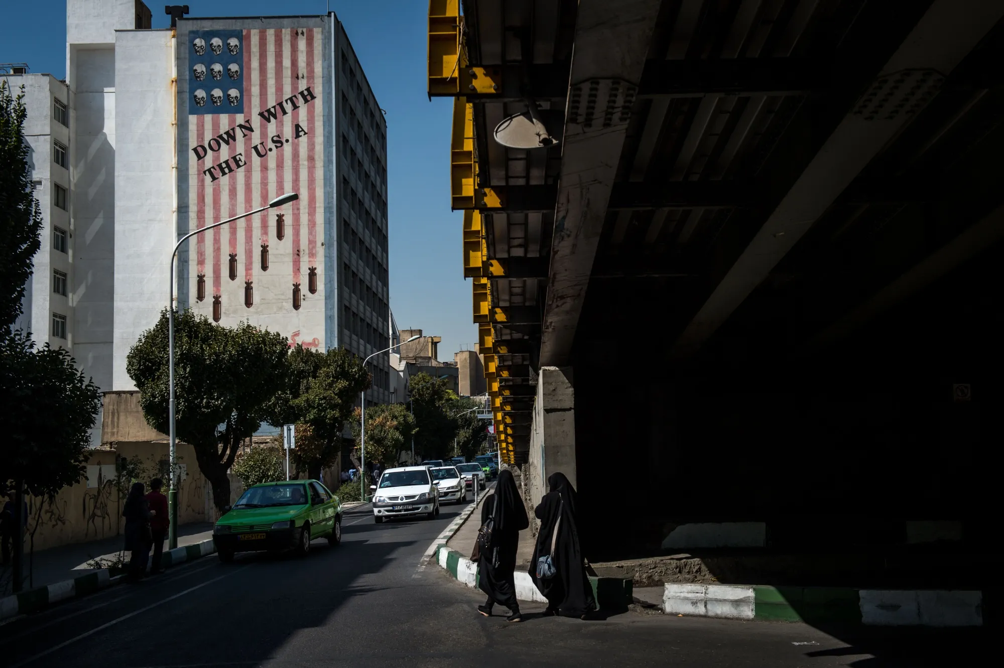 Pedestrians walk through a highway overpass near a wall mural reading 'Down With The U.S.A.' in Tehran.