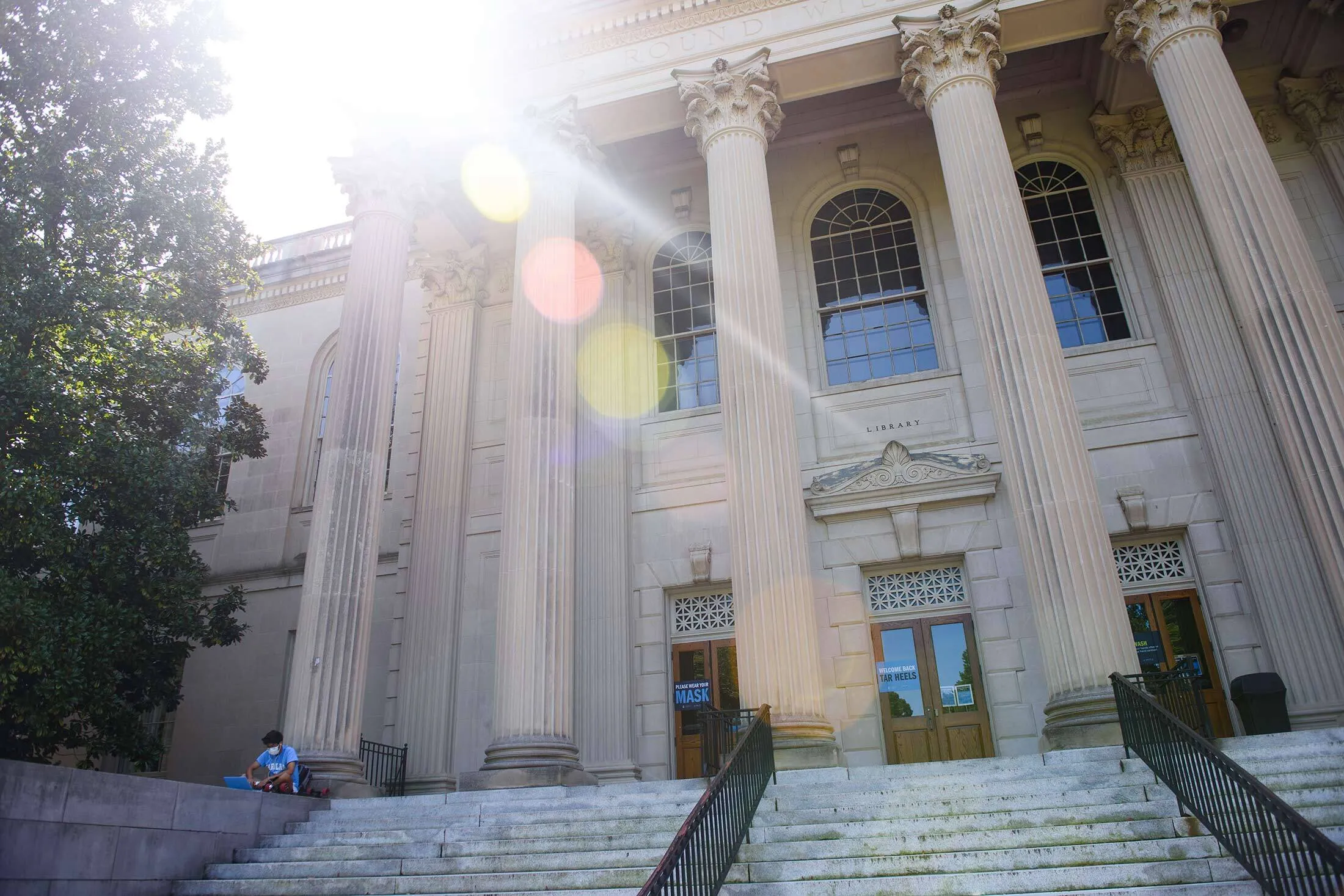 A masked student studies outside the closed Wilson Library on the campus of the University of North Carolina at Chapel Hill.