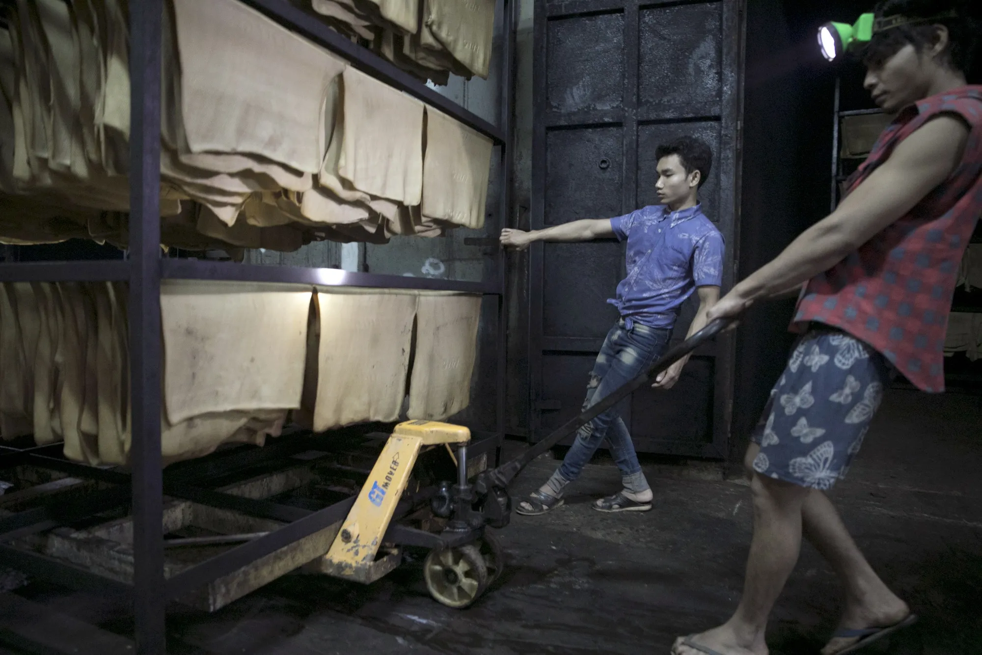 Workers use a pallet jack to move a rack of rubber latex sheets at a factory in Thailand in 2019.