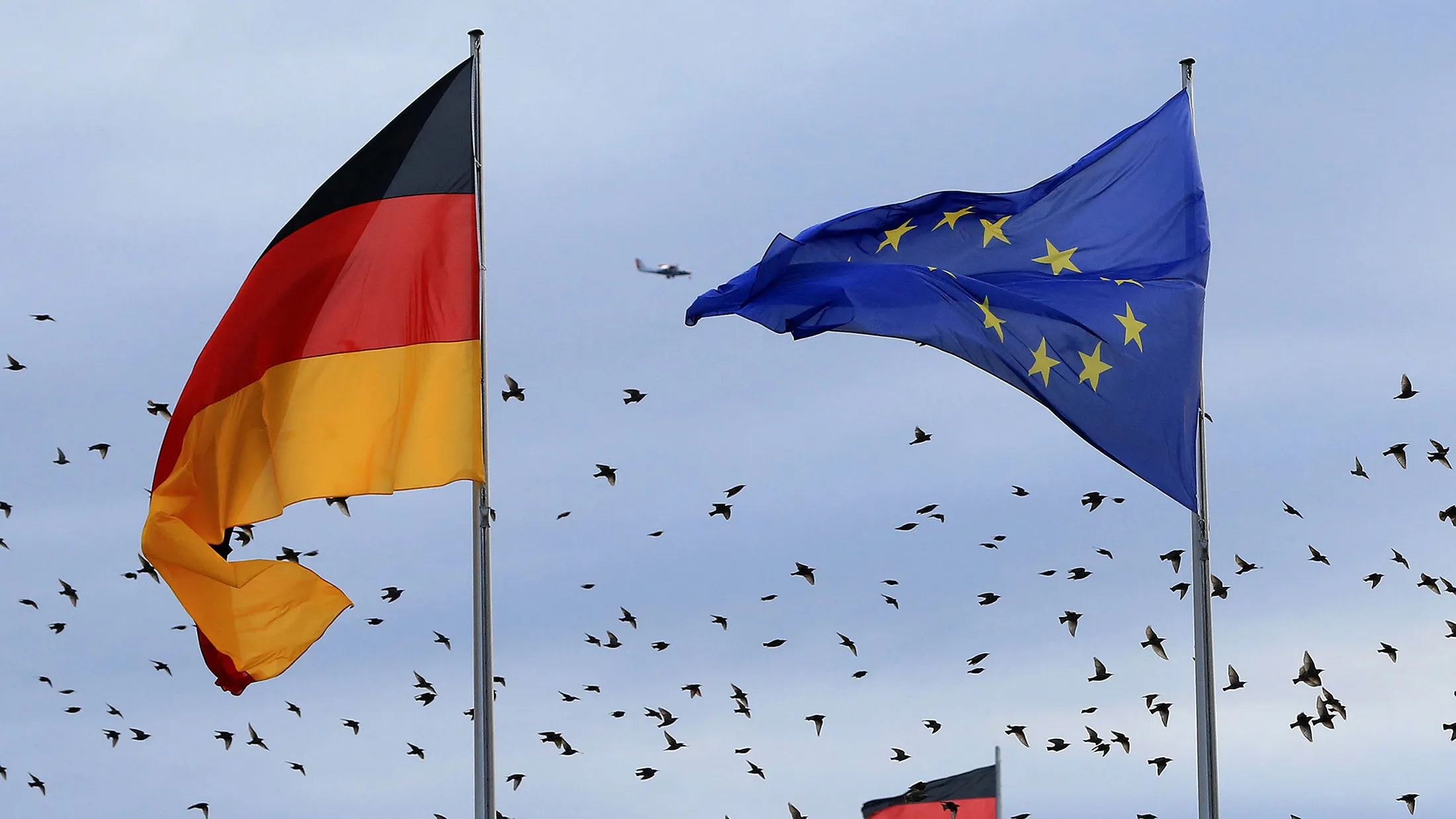 The German national flag flies beside a European Union (EU) flag as a flock of birds take flight over the Reichstag building in Berlin, Germany, on Nov. 18, 2016.
