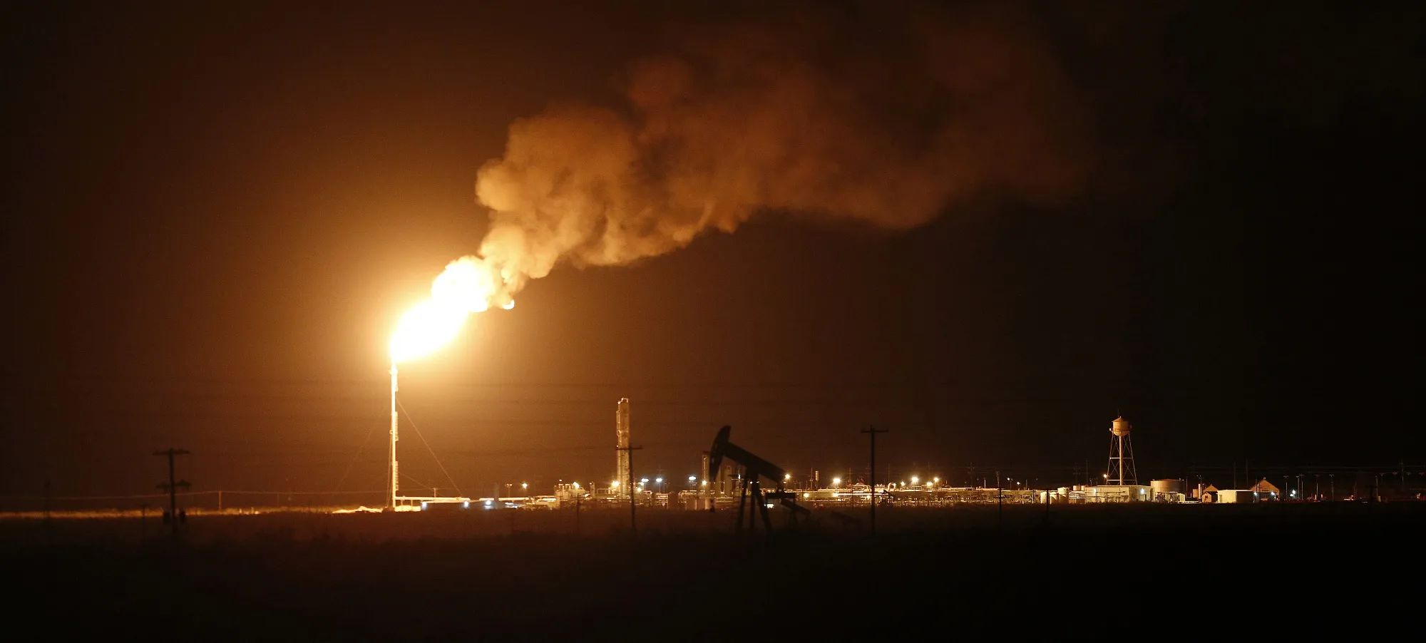 The silhouette of an electric oil pump jack is seen near a flare at night in the oil fields surrounding Midland, Texas.