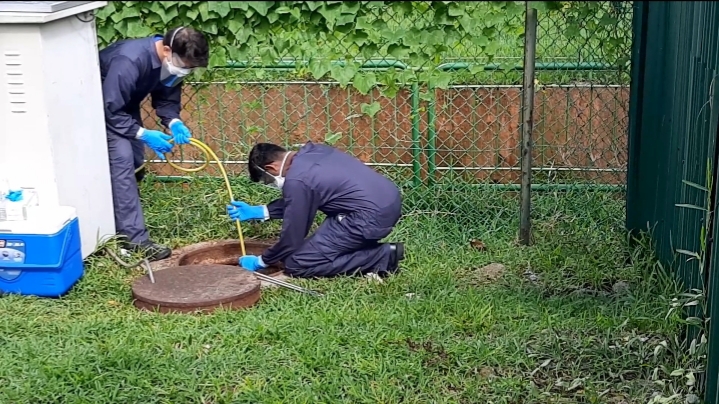 Scientists insert a rubber tube into the manhole outside a workers’ dormitory in Singapore to collect wastewater samples.