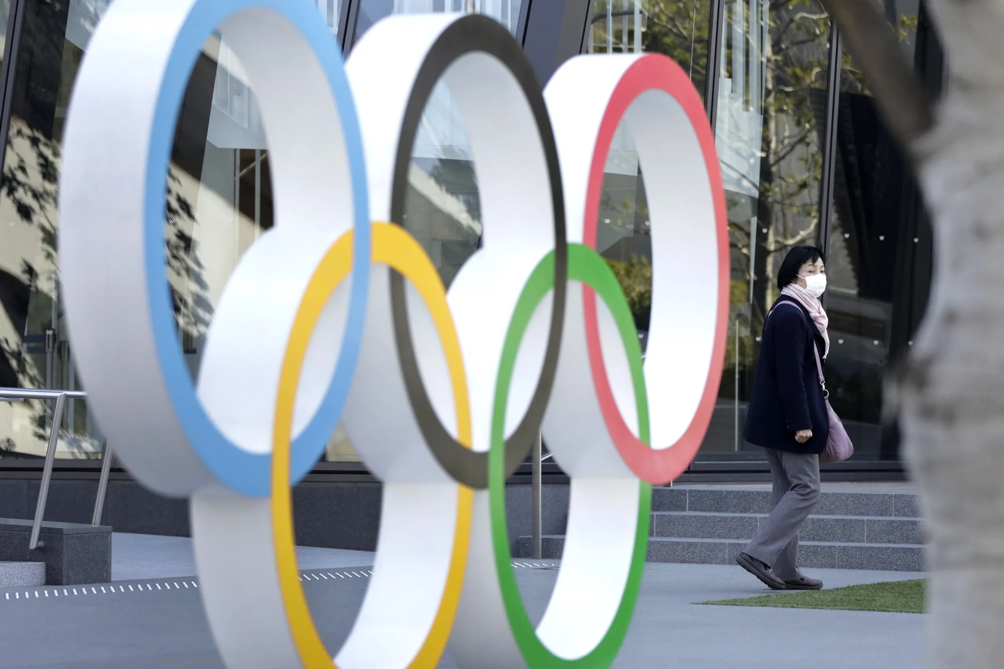 A pedestrian wearing a protective face mask walks past the Olympic rings installed outside the Japan Olympic Museum near the New National Stadium,&nbsp; in Tokyo, on March 11.