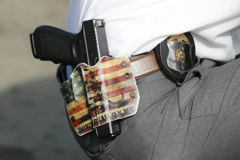 Wearing a holster bearing the phrase "DON'T TREAD ON ME," a Dayton police officer performs a grid search beside a makeshift memorial for victims of the August 4 mass shooting in Dayton, Ohio. August 6, 2019.