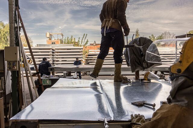 Employees work outside with sheets of metal at the EcoSan factory. 