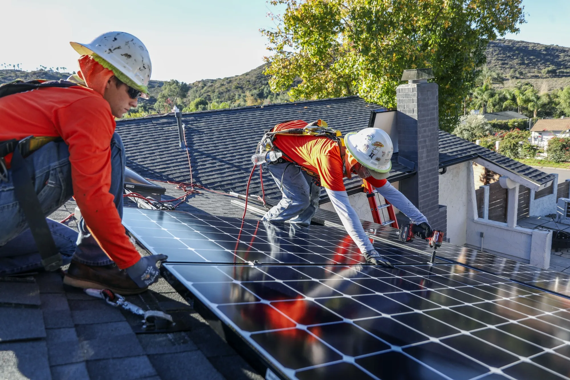 Workers install solar panels on the rooftop of a home in Poway, California.