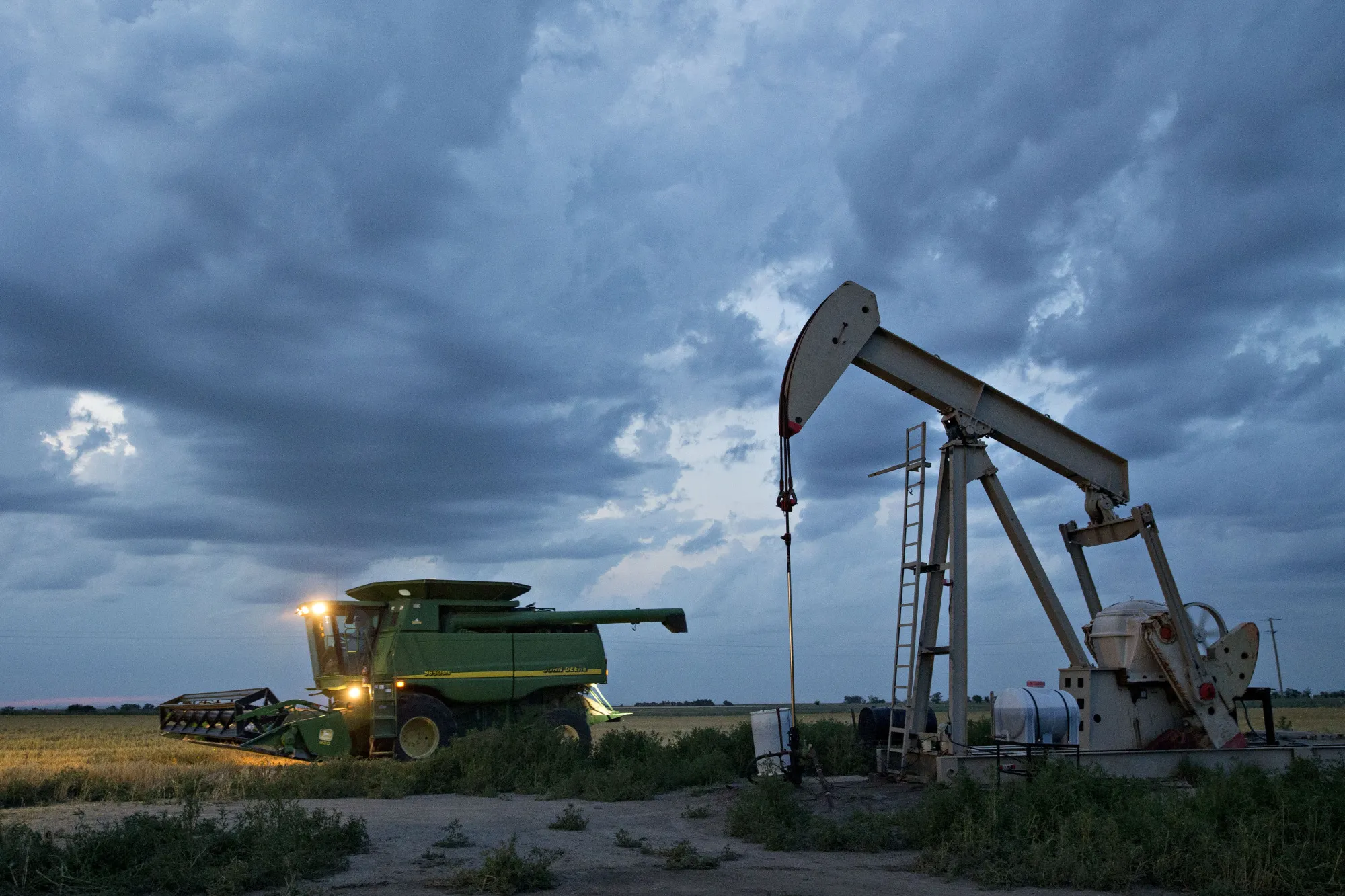 A&nbsp;combine harvester drives past a pumpjack in an&nbsp;oil field&nbsp;in Plainville, Kansas.