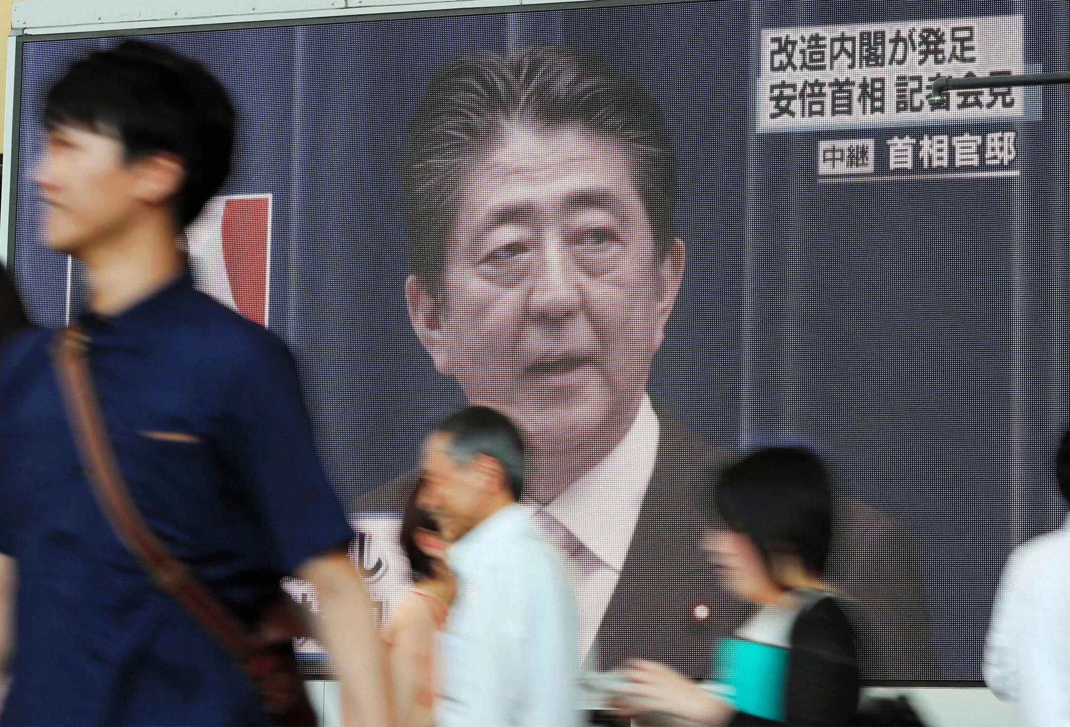 People walk past a giant screen broadcasting the news of Prime Minister Shinzo Abe reshuffling his cabinet on August 3, 2017 in Osaka, Japan.
