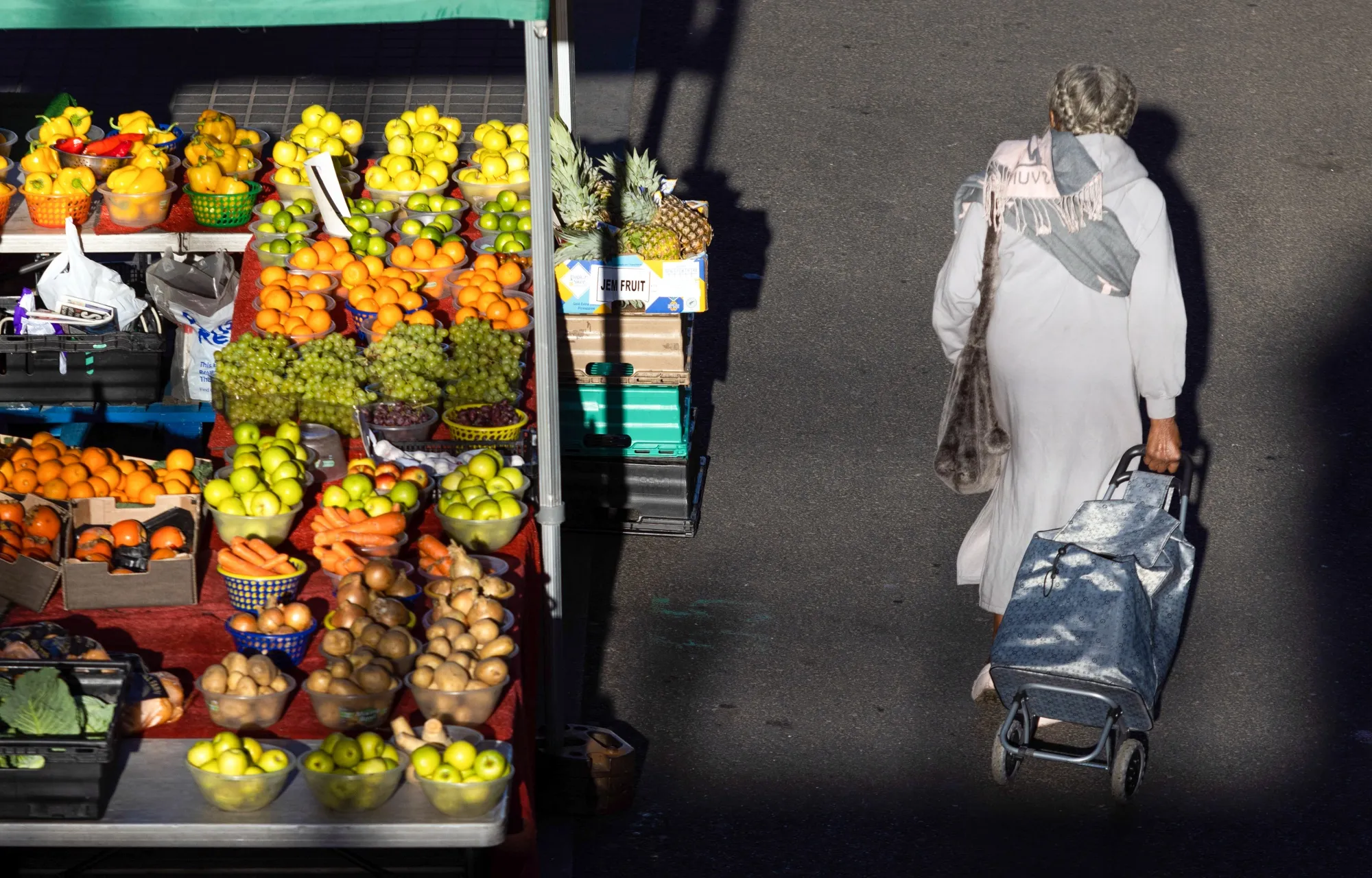 A shopper passes a market stall selling fresh fruit and vegetables in Croydon, Greater London.