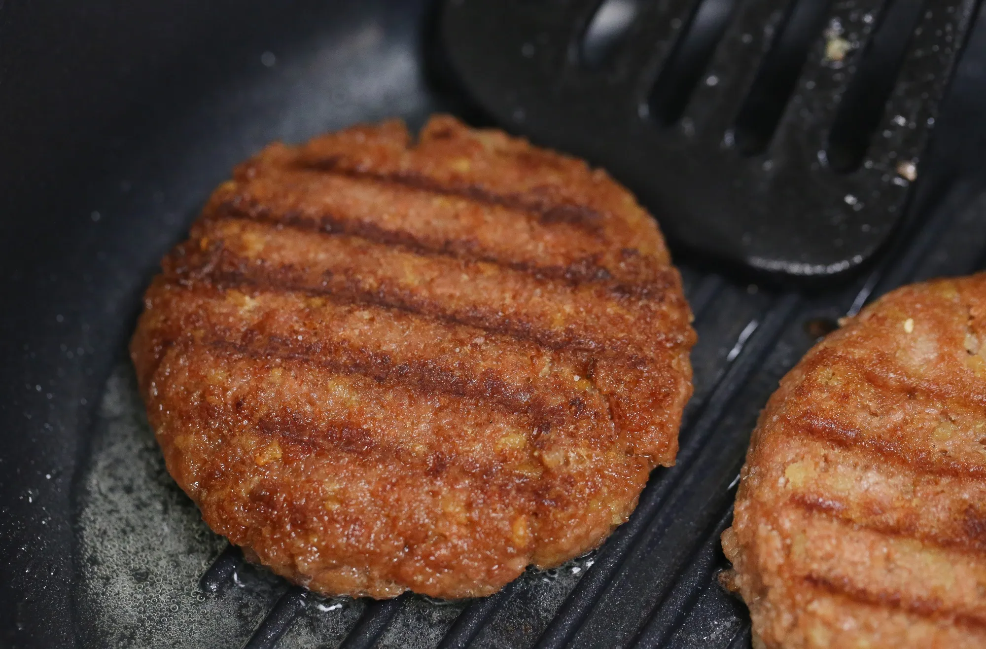A vegetable-based burger patty cooks on a griddle pan.