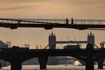 Commuters cross the Millennium Bridge in view of Tower Bridge in London.