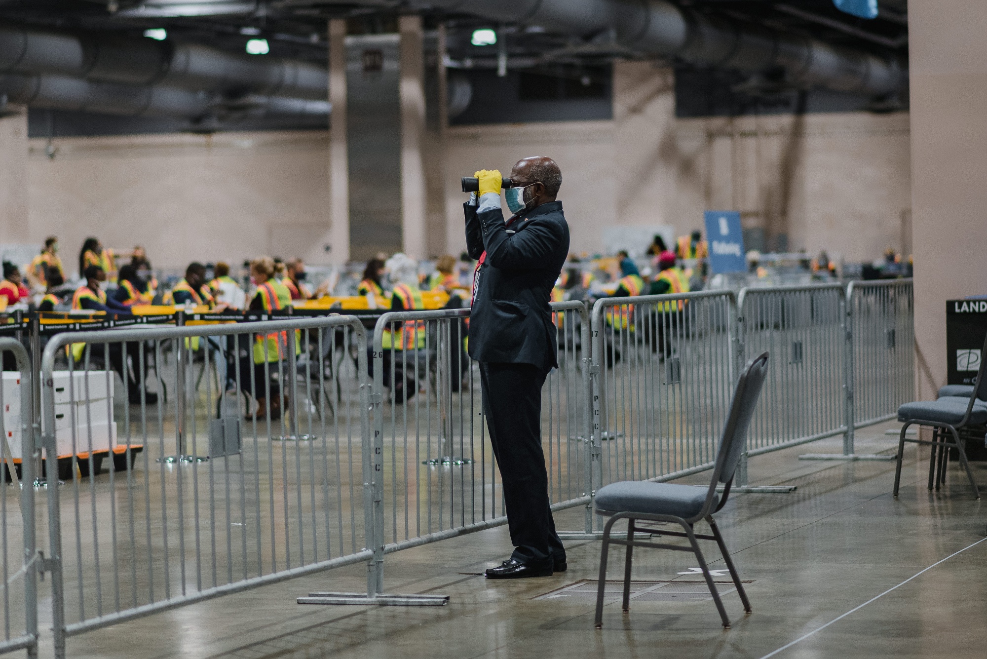 An official poll watcher uses binoculars as workers count ballots for the 2020 presidential election at the Philadelphia Convention Center on Nov. 3, 2020.