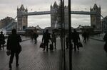A reflection of Tower Bridge sits in a window as pedestrians walk through the More London office space in London.
